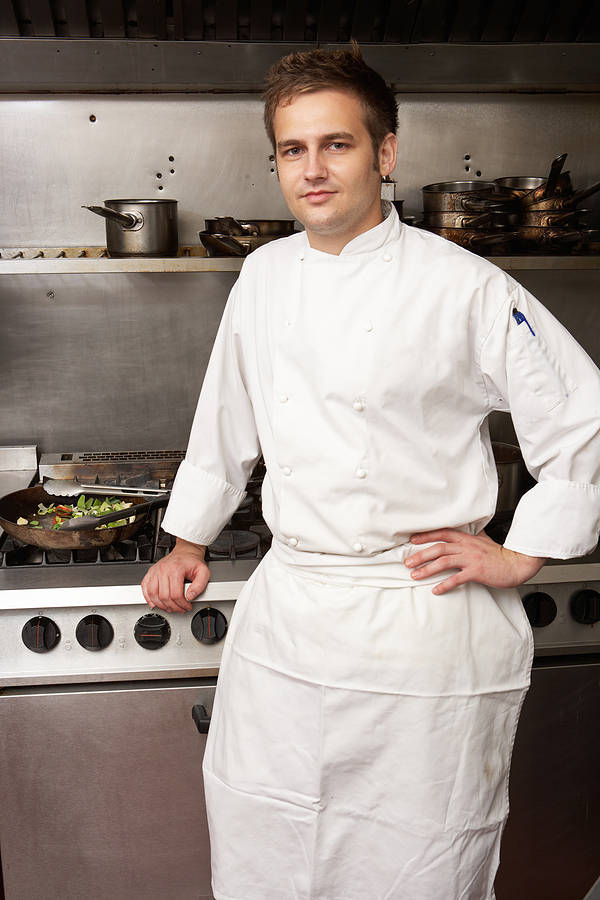 male chef in cooks clothing in front of stove
